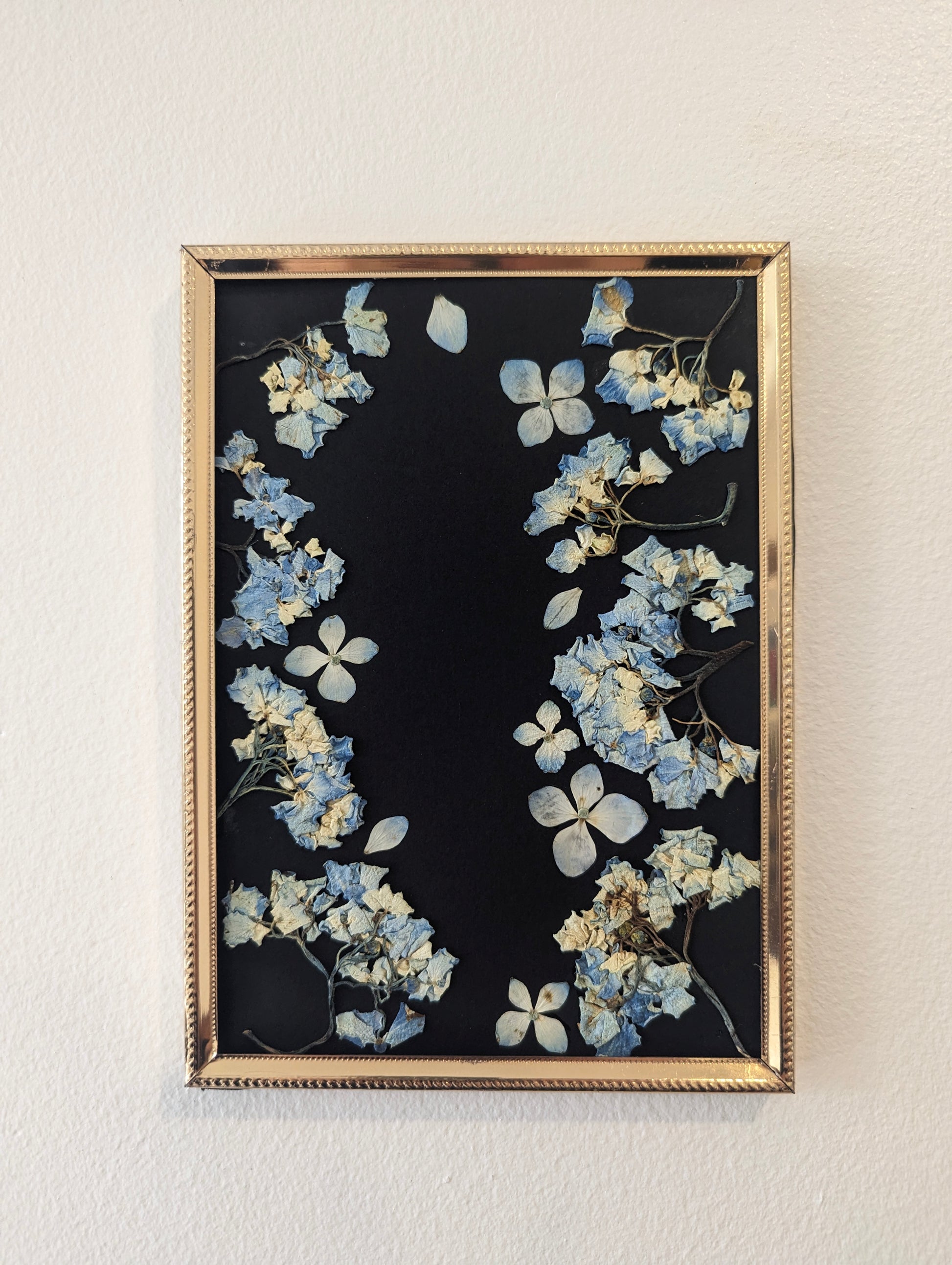 Pressed flower arrangement displayed in a heart shape on a canvas.