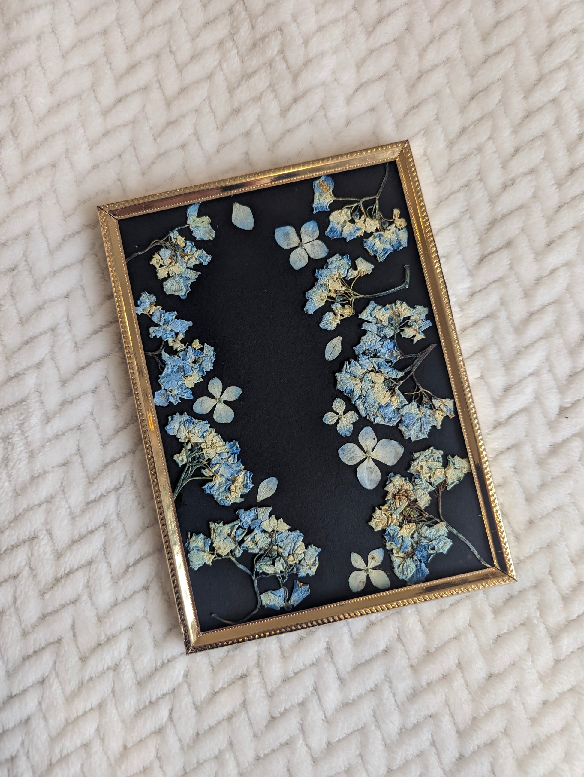 Pressed flower arrangement displayed in a heart shape on a canvas.